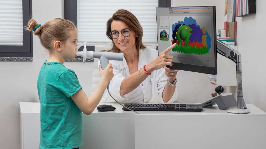 Spirometrische Untersuchung mit einem Kind, zur Unterstützung wird an einem Bildschirm die Kinderanimation "Schnaufi der Drache" gezeigt