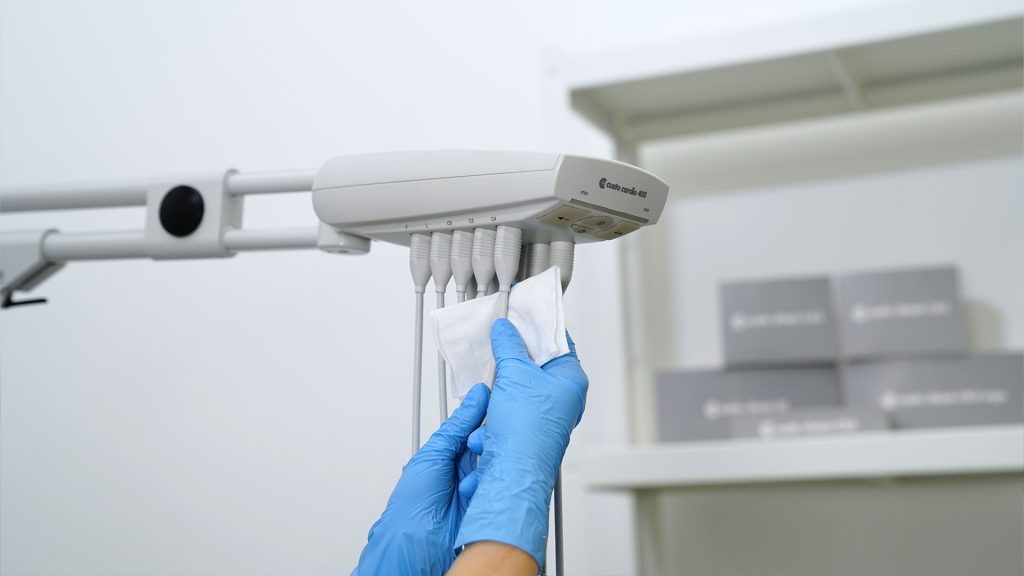 custo cardio 400 an Gerätearm, wird von Hand in Einmalhandschuhen mit einem Reinigungstuch gereinigt