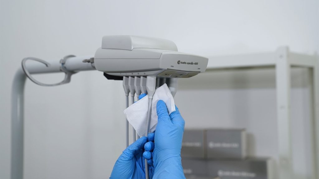 custo cardio 400 accu an Gerätearm, wird von Hand in Einmalhandschuhen mit einem Reinigungstuch gereinigt