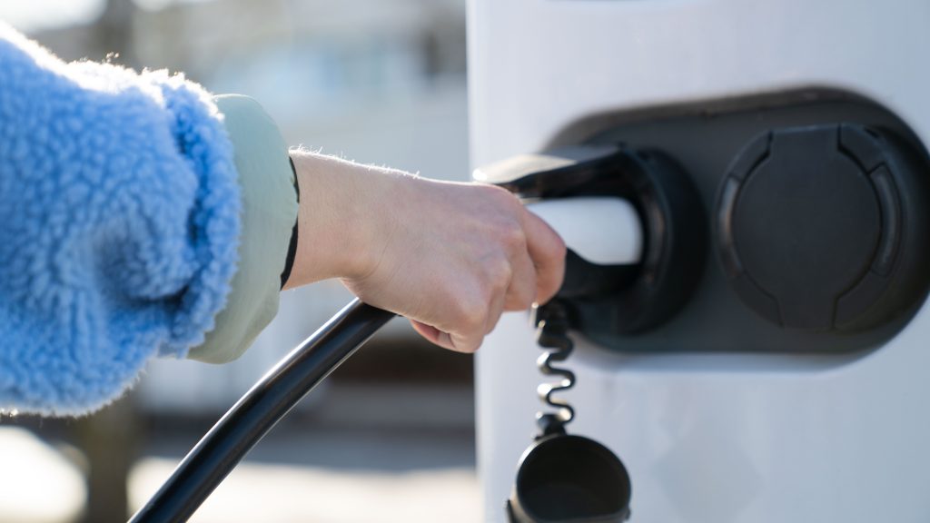 Mano sul cavo di ricarica: ricarica di un veicolo elettrico, dettaglio della stazione di ricarica e del cavo
